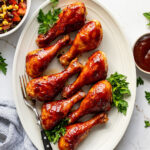 Chicken drumsticks covered in glossy barbecue sauce laid out on an oval dish.