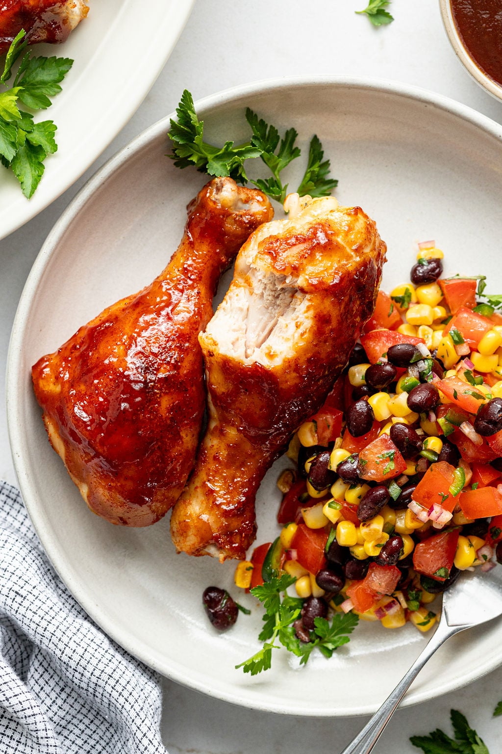 A half-eaten chicken drumstick next to corn, black beans, and chopped tomatoes on a plate.
