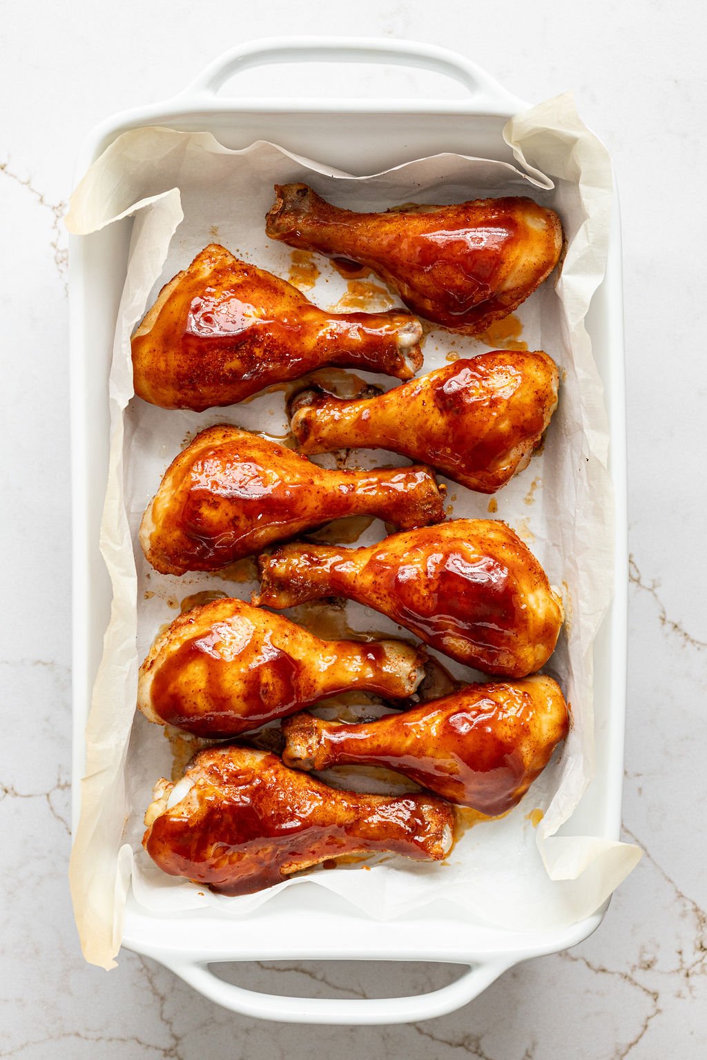 Baked chicken drumsticks covered with glossy barbecue sauce in a dish.