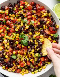 A hand dipping a round chip into a bowl of black bean and corn salsa.