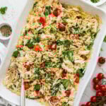 A white baking dish filled with creamy baked chicken and orzo with cherry tomatoes and parsley.