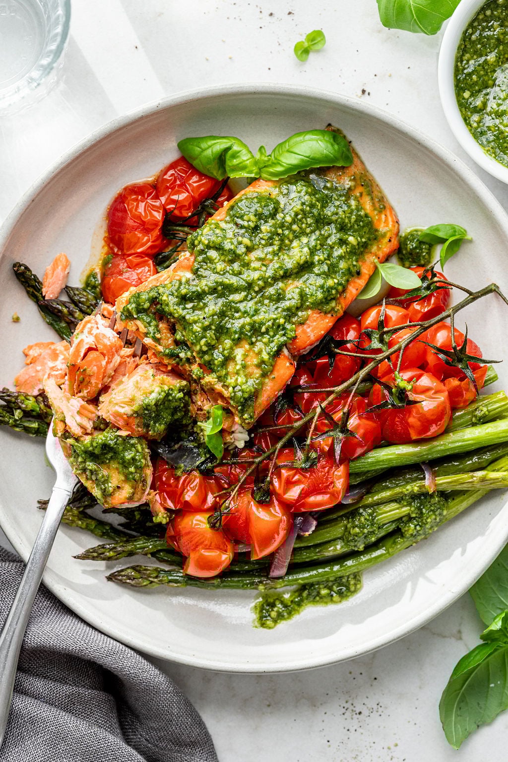 A partially eaten salmon filet topped with creamy pesto on roasted tomatoes and asparagus on a plate.