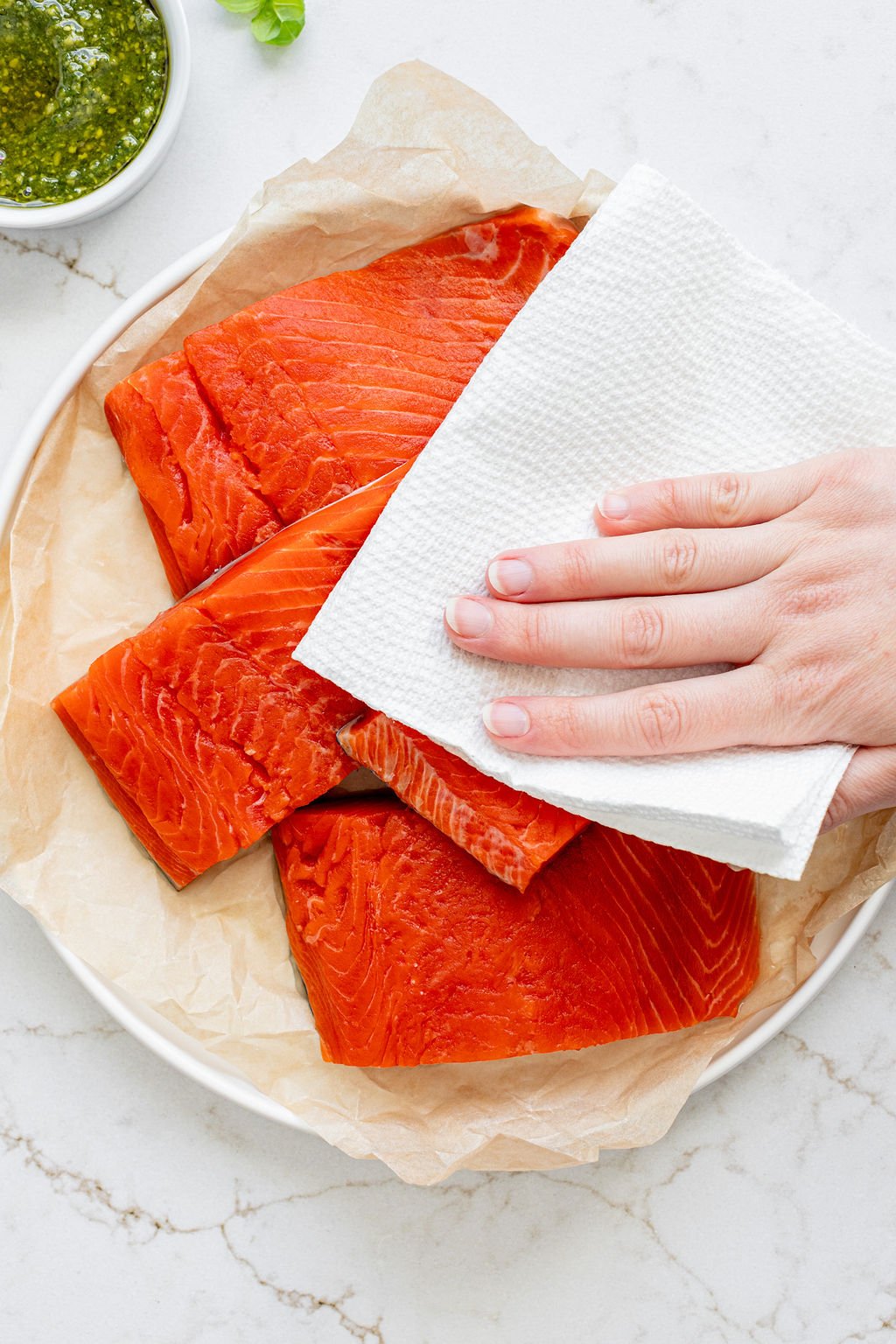 A hand patting raw salmon filets with a paper towel.