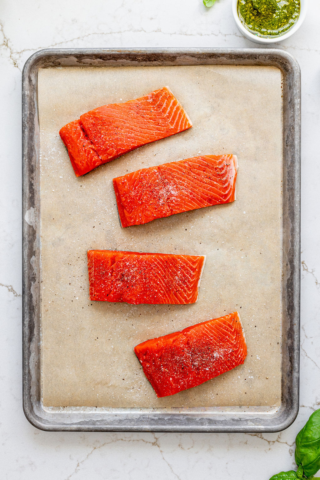 Four raw salmon filets on a baking sheet sprinkled with salt and pepper.