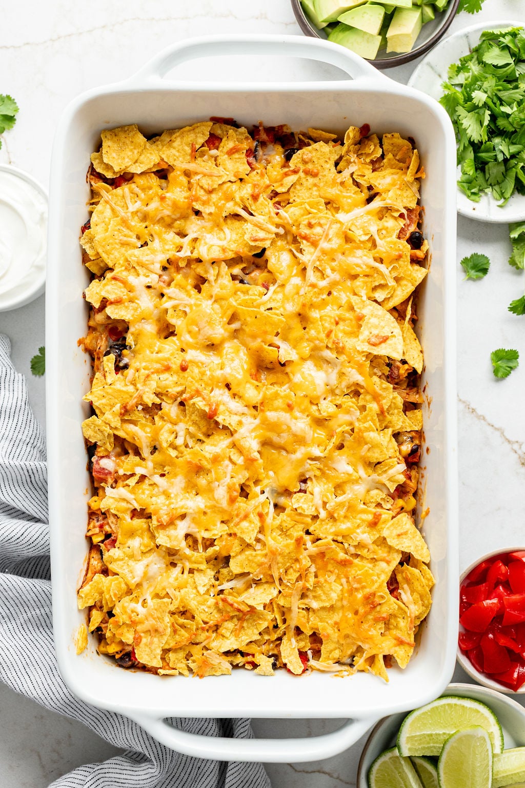Melted shredded cheese on top of crushed corn chips in a baking dish.