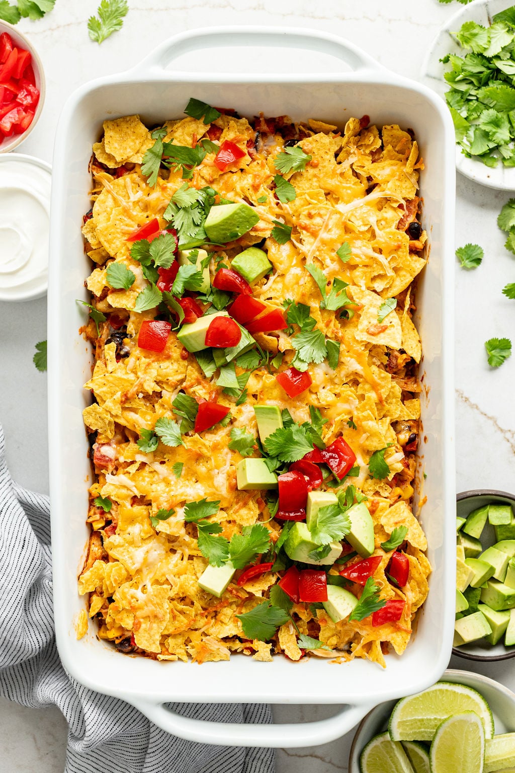 Cilantro, chopped avocado, and diced tomatoes on a baking dish with crushed corn chips and melted cheese.