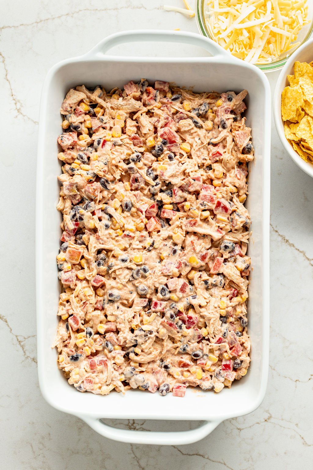 Creamy shredded chicken, black beans, diced tomatoes, and corn in a baking dish.