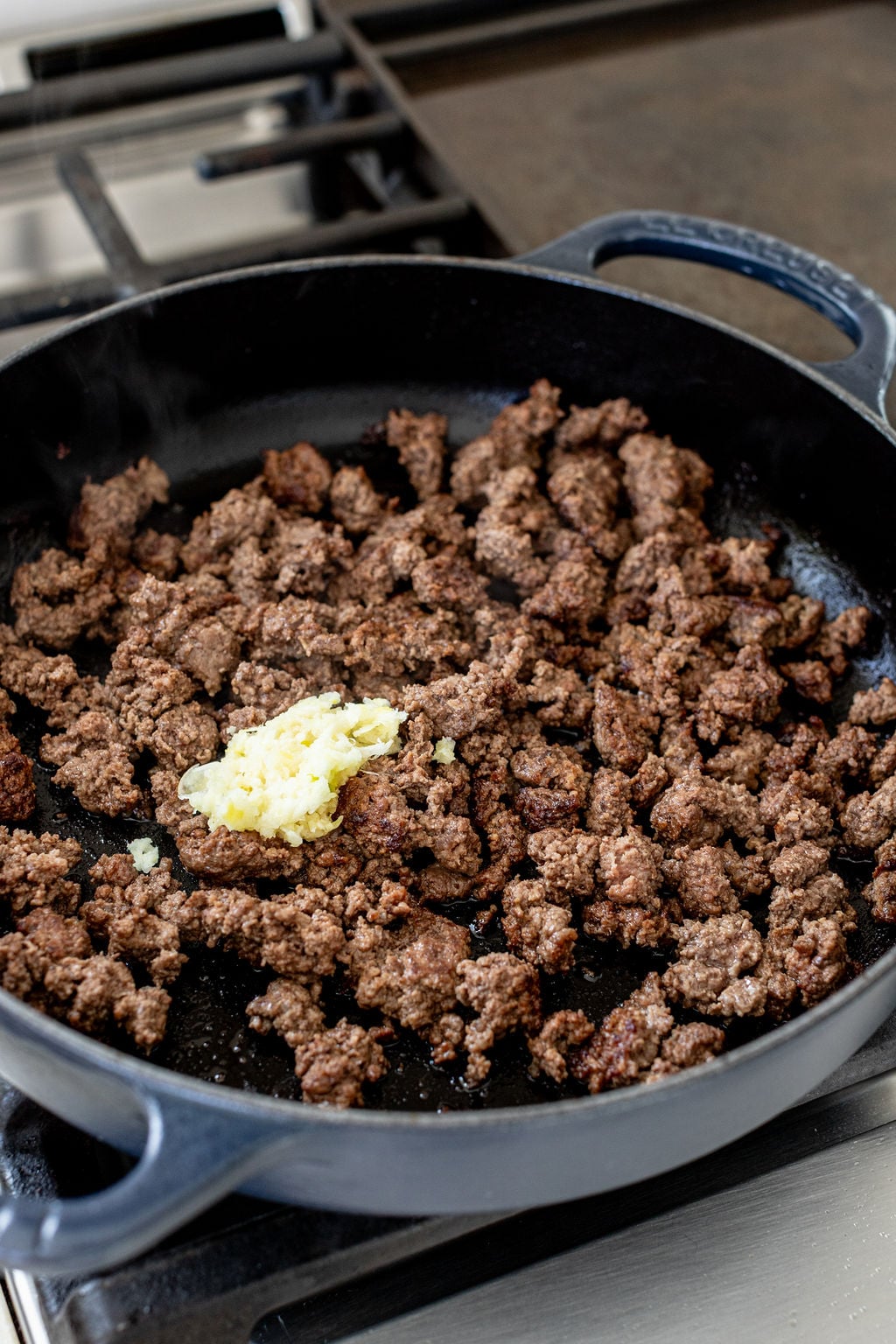 Cooked ground beef crumbles in a skillet with minced garlic.