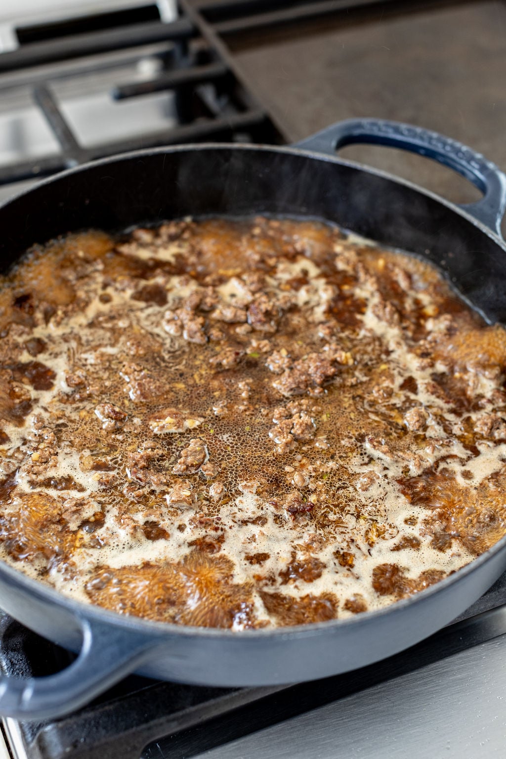 Cooked. crumbled ground beef and broth simmering in a skillet on a stove.