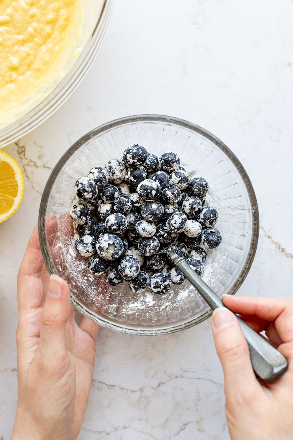 A hand tossing fresh blueberries in a bowl with flour.