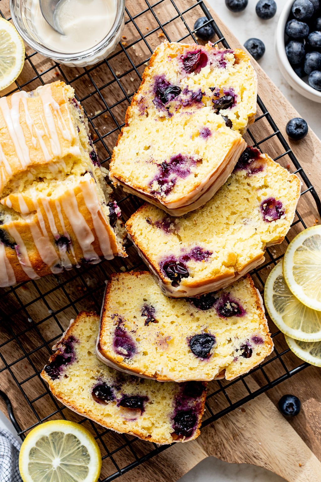 Four slices of glazed lemon blueberry loaf cake on a wooden cutting board.