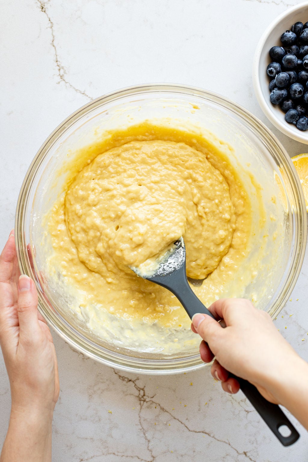 A hand stirring yellow cake batter in a large bowl with a spoon.