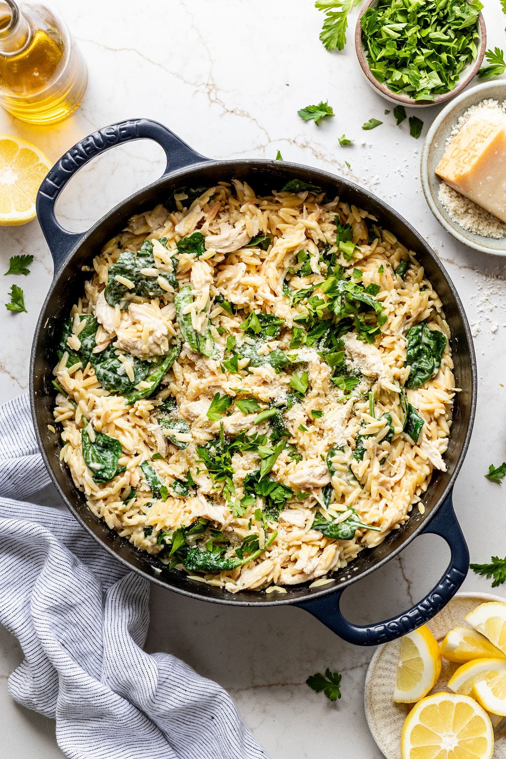 Creamy cooked orzo, spinach, and shredded chicken in a large skillet next to lemon slices.