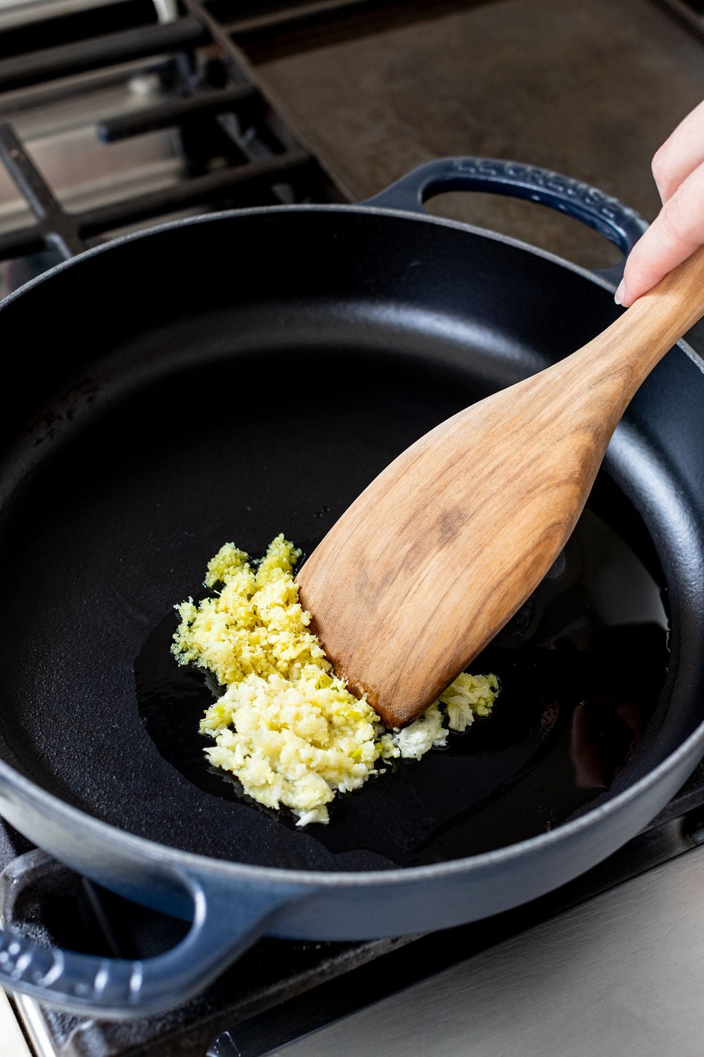 A wooden spoon stirring minced garlic in a pan with oil.