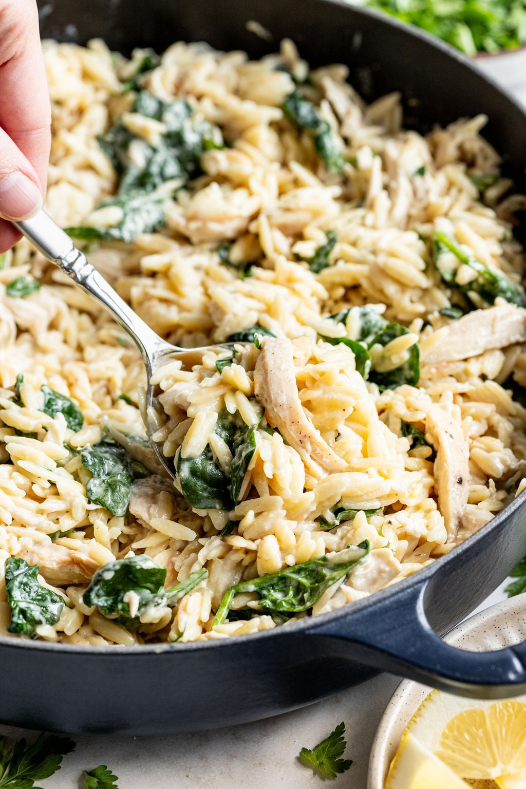 A hand scooping a spoonful of creamy cooked orzo, chicken, spinach, parmesan, and cream cheese.