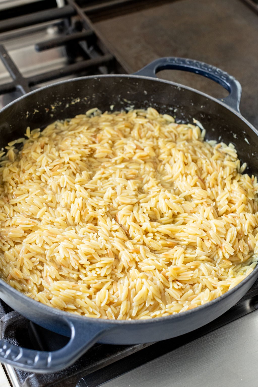 Cooked creamy orzo in a large skillet on a stove.