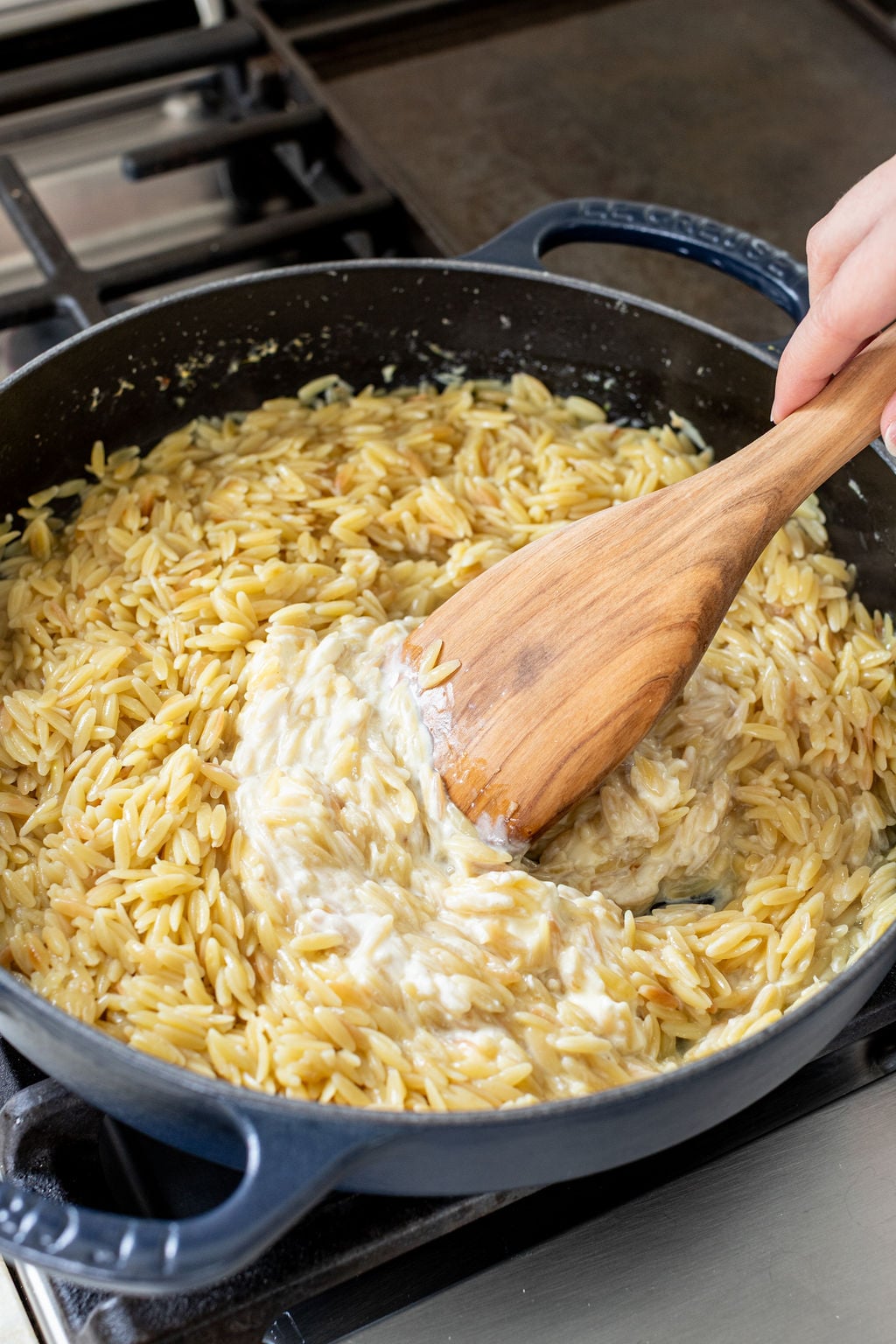 A wooden spoon stirring melted cream cheese into creamy orzo.