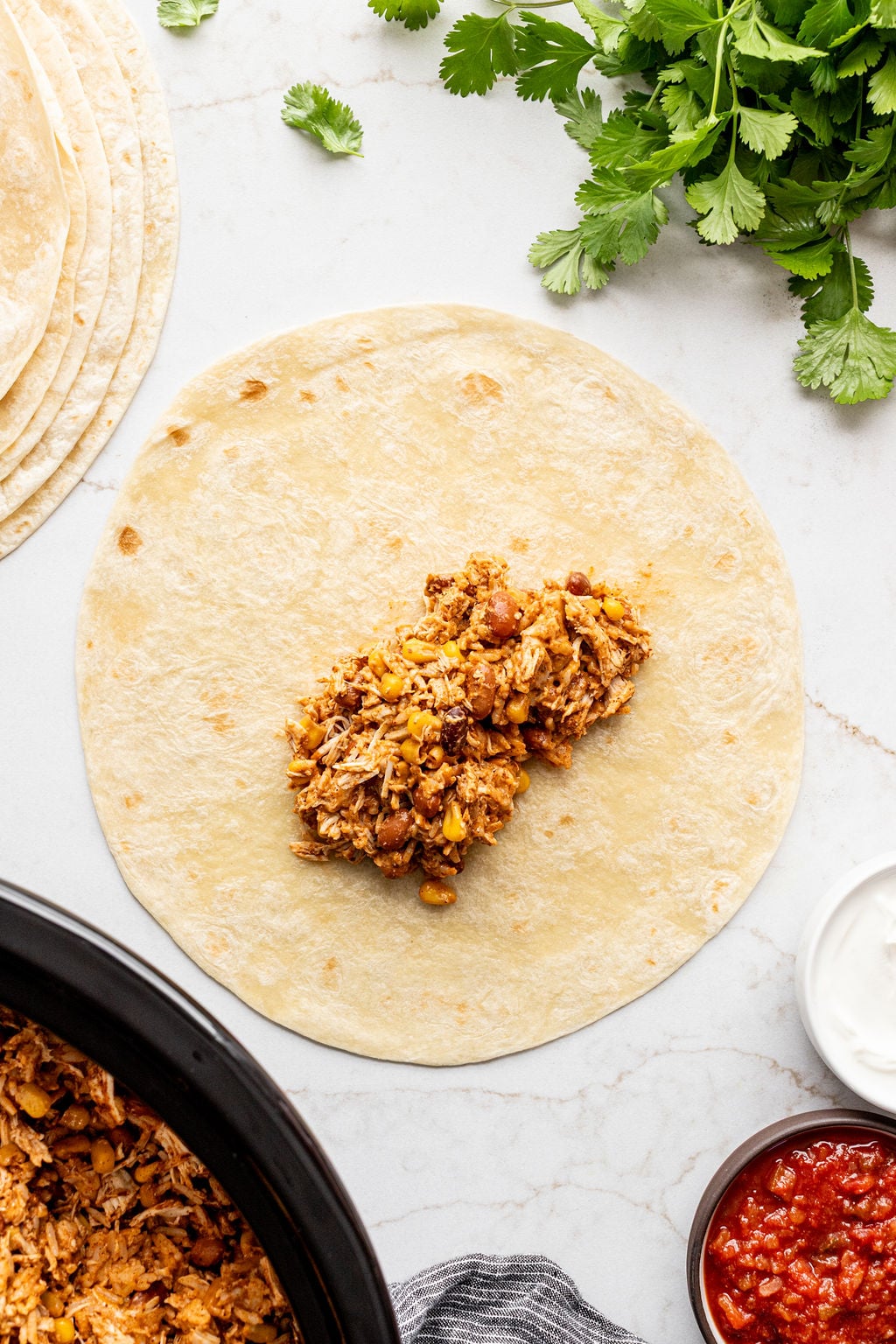 A flour tortilla topped with saucy shredded chicken, corn, and beans.