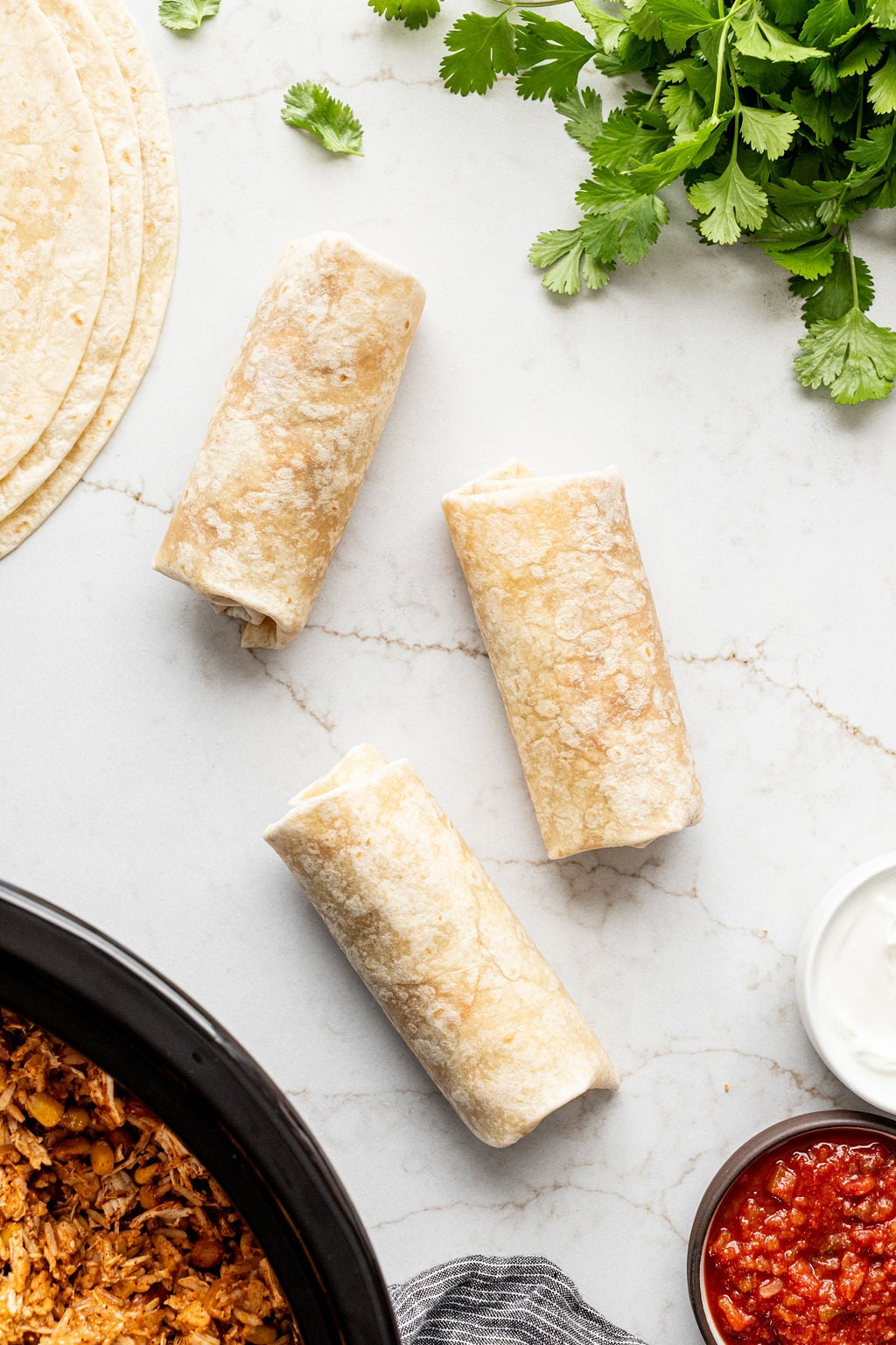 Three rolled burritos on a table.