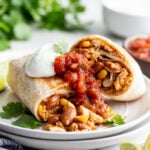 Two halves of a chicken burrito stacked on a plate topped with sour cream and salsa.