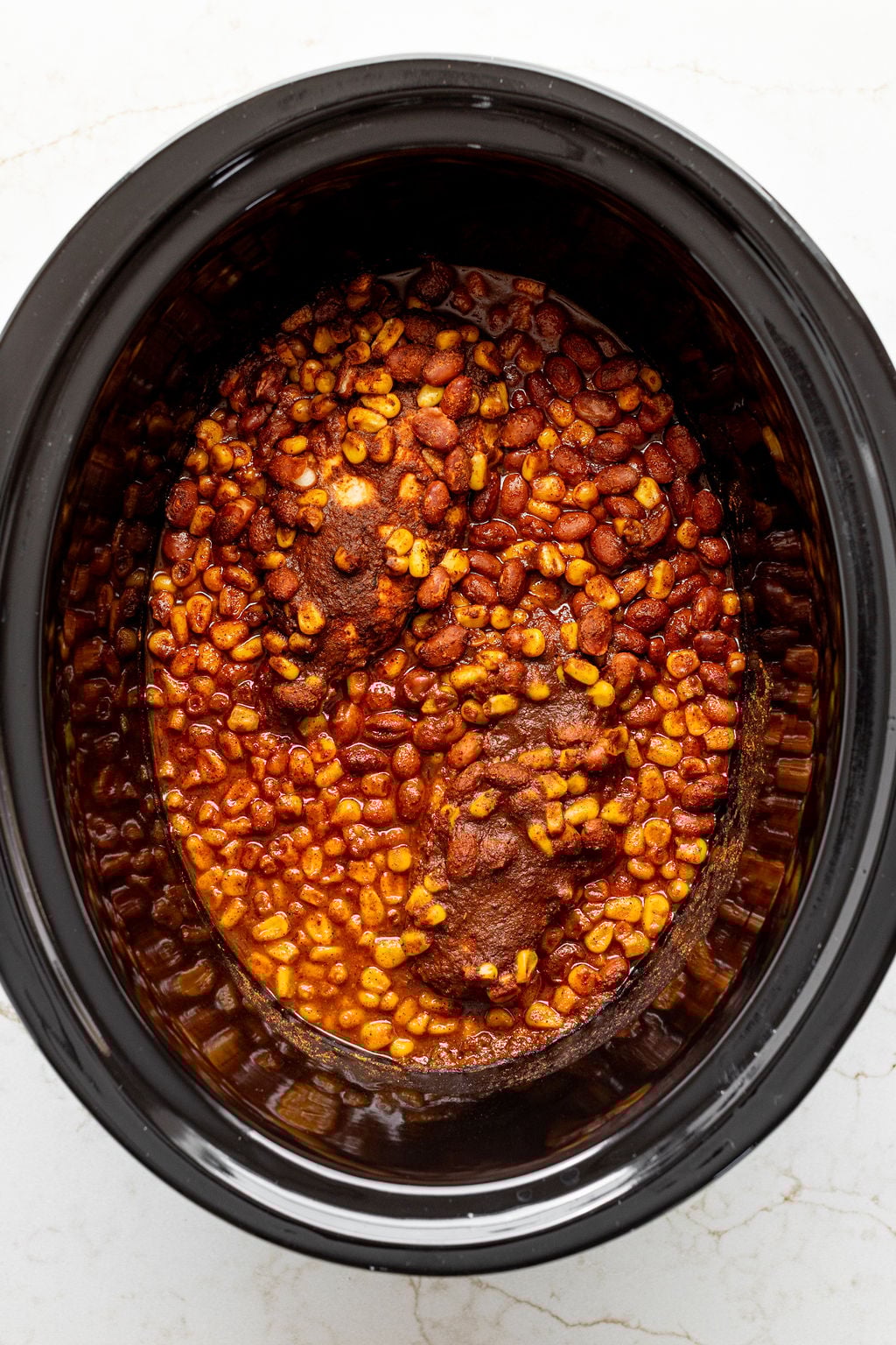 Spices, beans, corn, chicken, and enchilada sauce mixed in a crockpot.