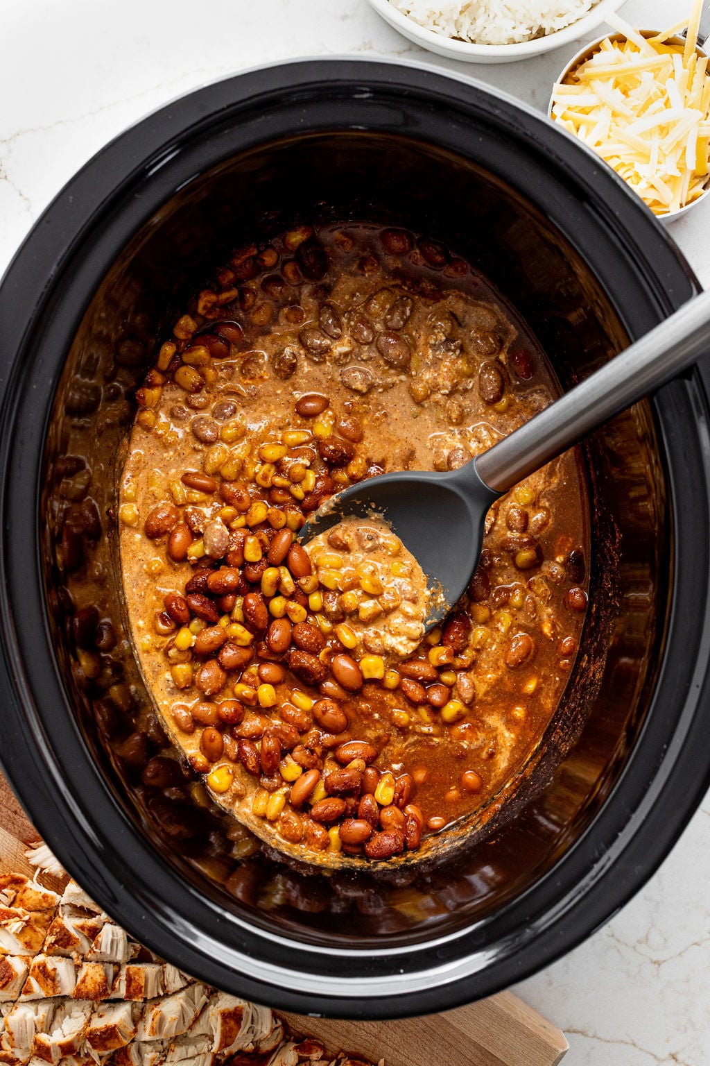 A spoon mixing a creamy blend of beans, corn, enchilada sauce, and taco seasoning.