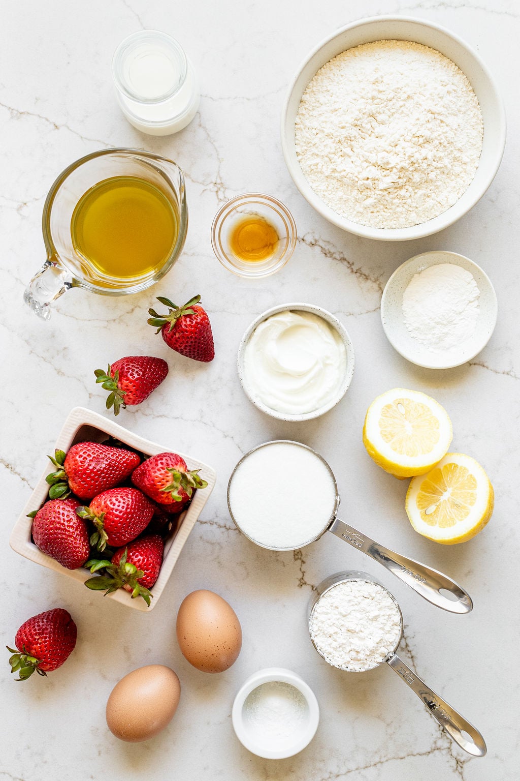 Bowls of sugar, flour, salt, strawberries, vanilla, Greek yogurt, baking powder, and oil on a table.