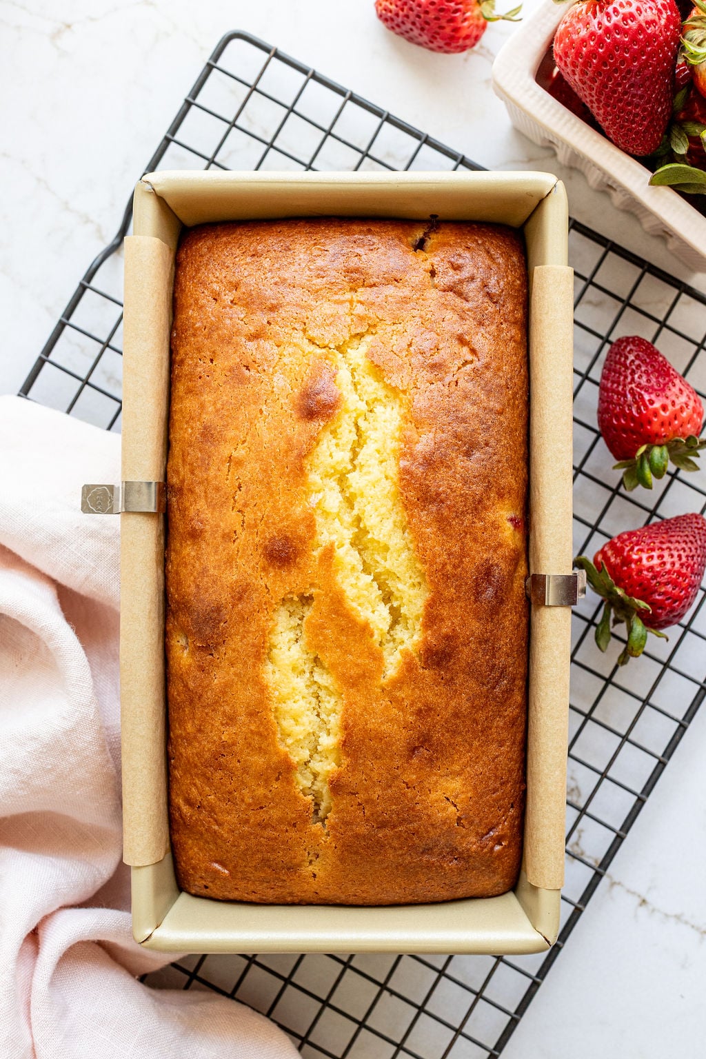 A baked loaf of cake in a loaf pan on a cooling rack.