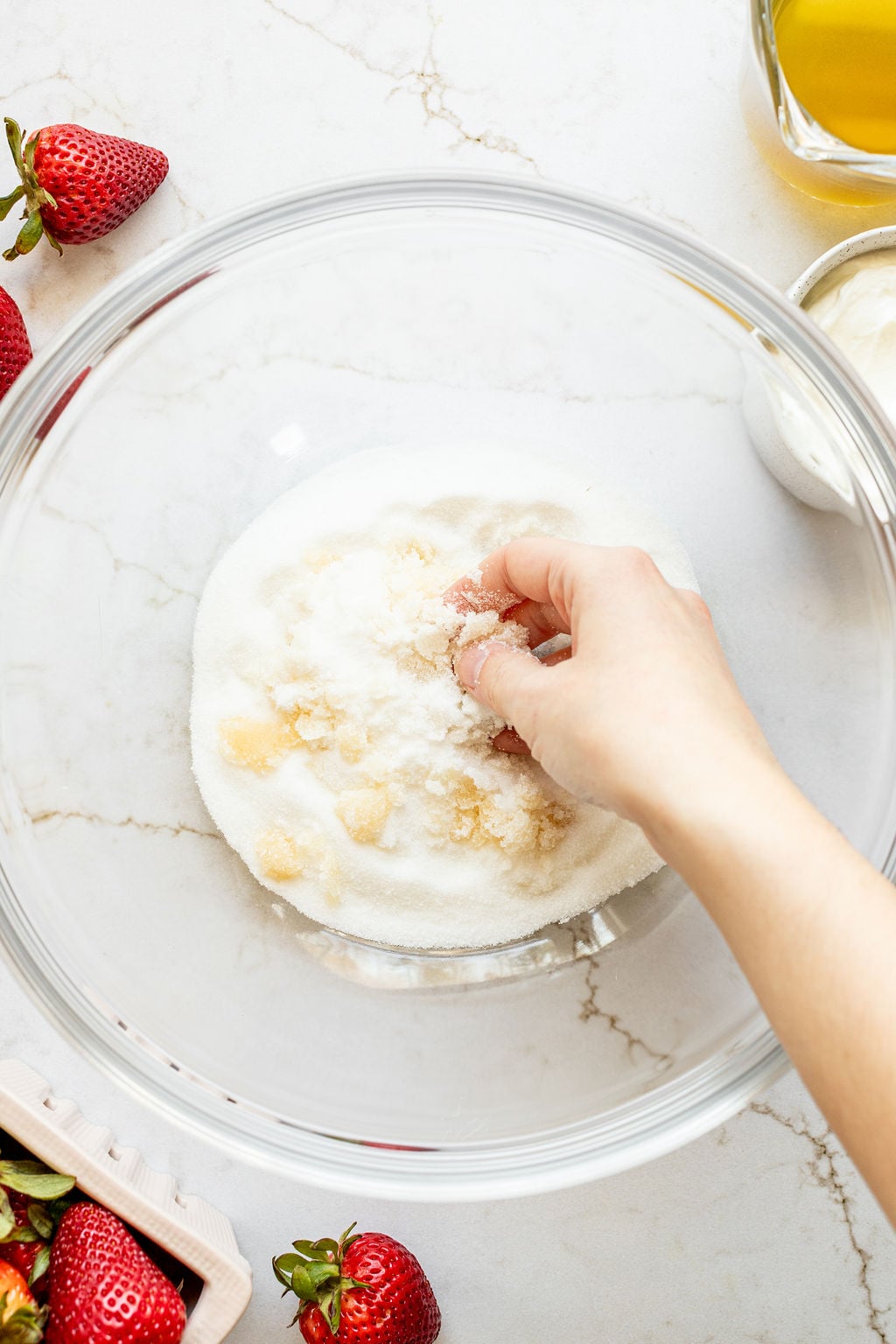 A hand rubbing vanilla extract and sugar in a bowl.