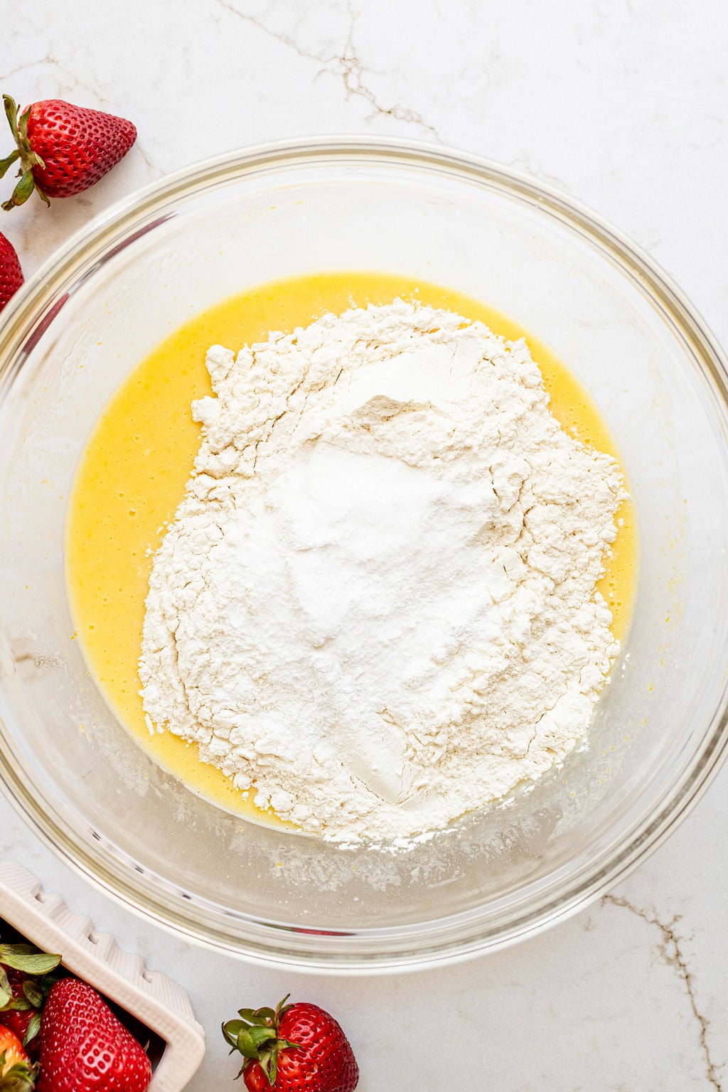 Flour sitting on top of a yellow mixture in a mixing bowl.