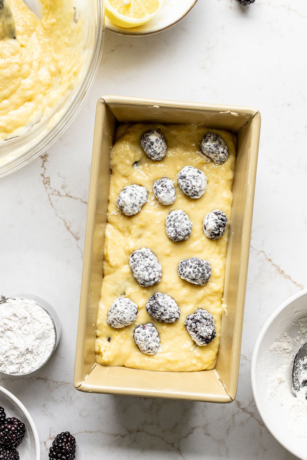 Yellow cake batter in a loaf pan with flour-coated blackberries on top.
