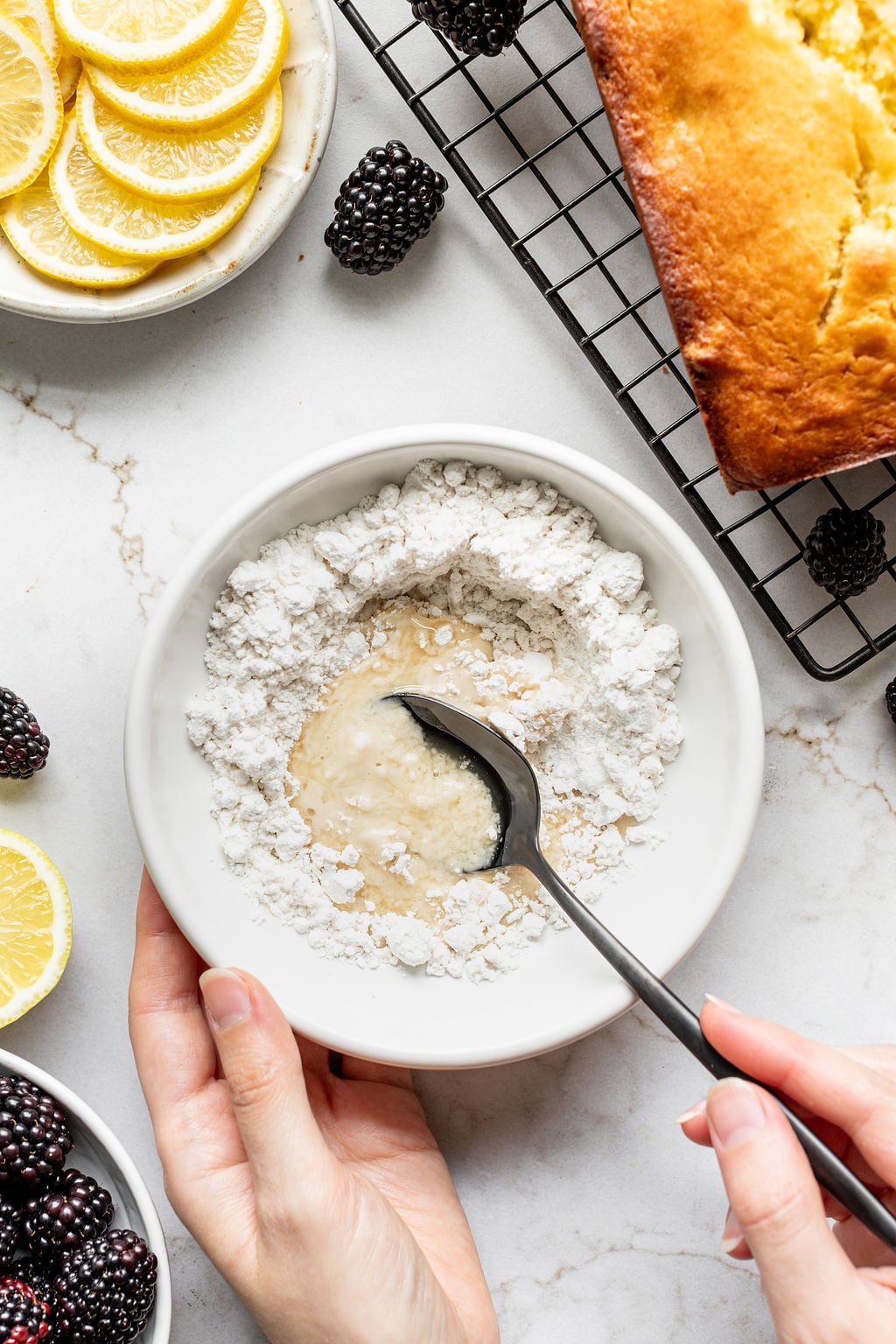 A hand stirring lemon juice and powdered sugar in a small bowl.