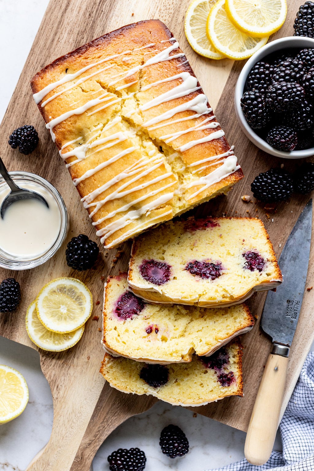 Sliced blackberry loaf cake on a wooden board next to a knife.