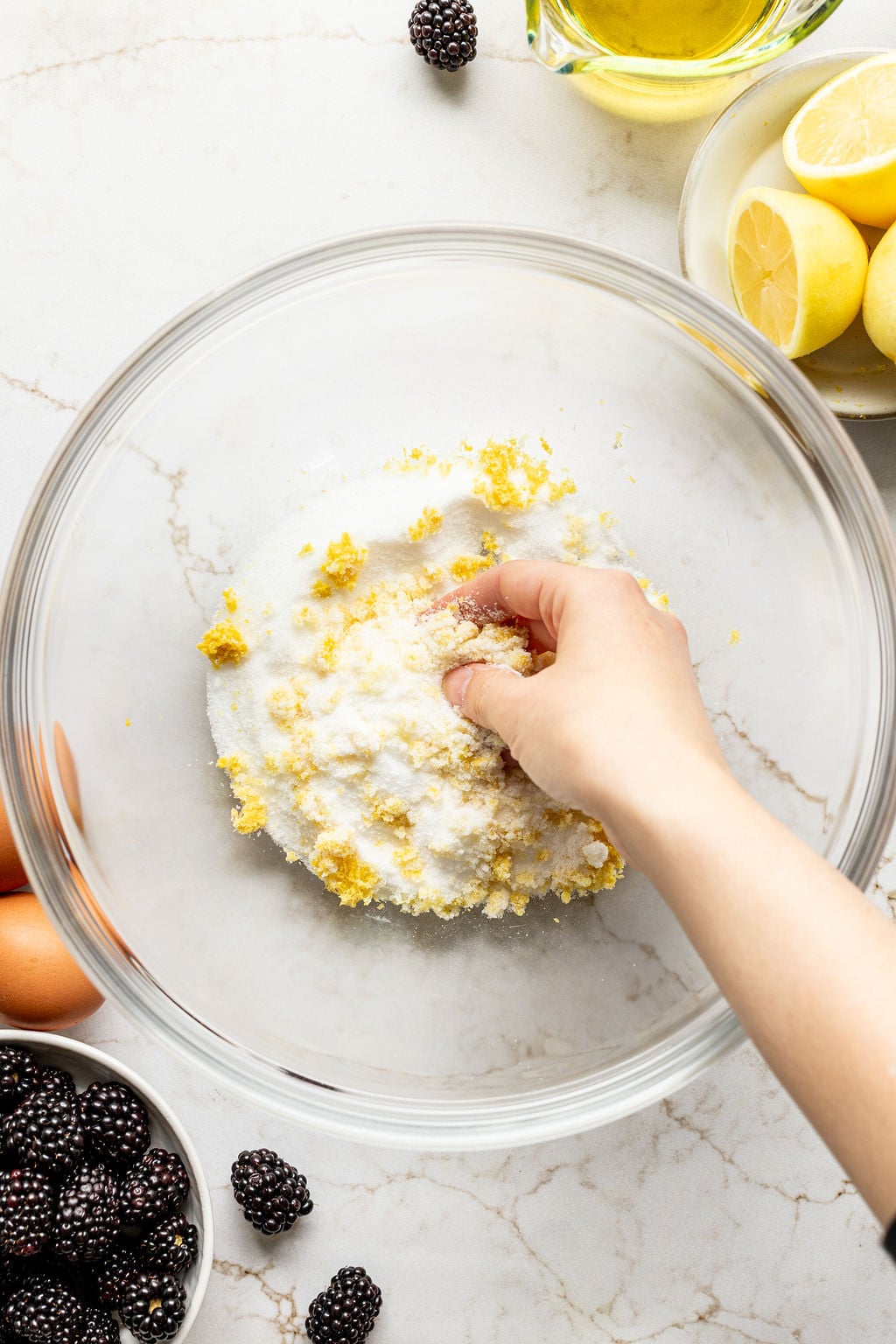 A hand rubbing lemon zest and granulated sugar together in a bowl.