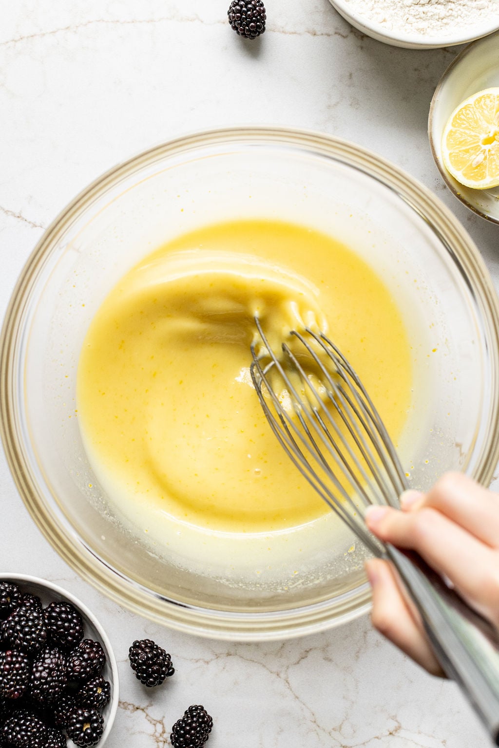 A hand whisking a smooth, creamy, yellow mixture in a glass bowl.