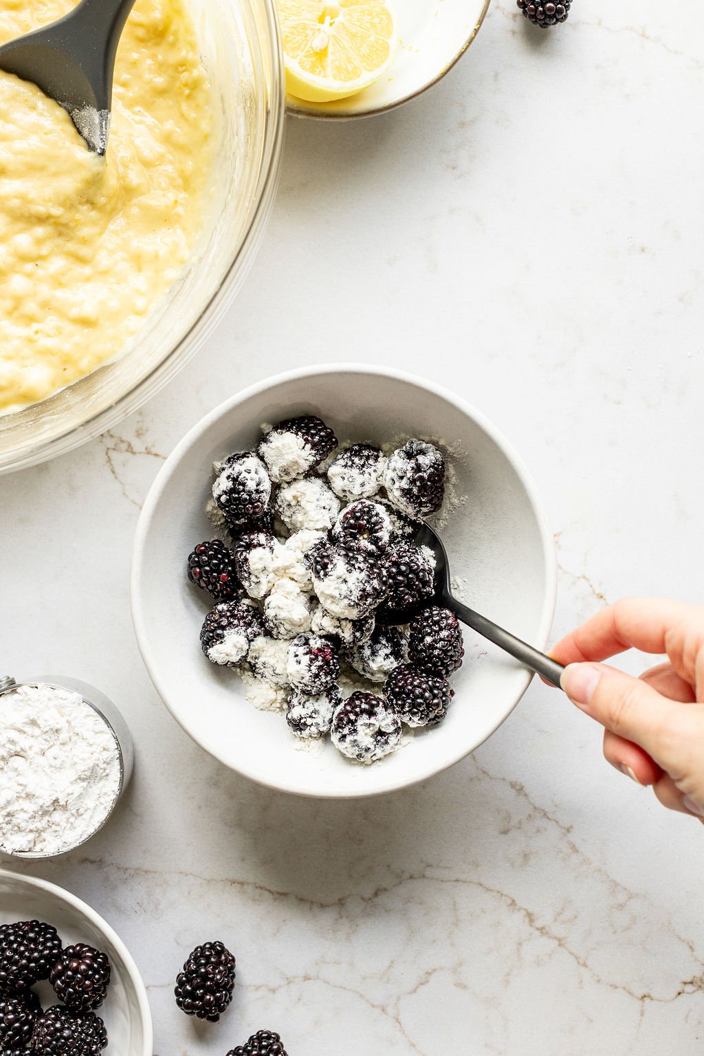 A hand tossing blackberries in flour with a spoon.