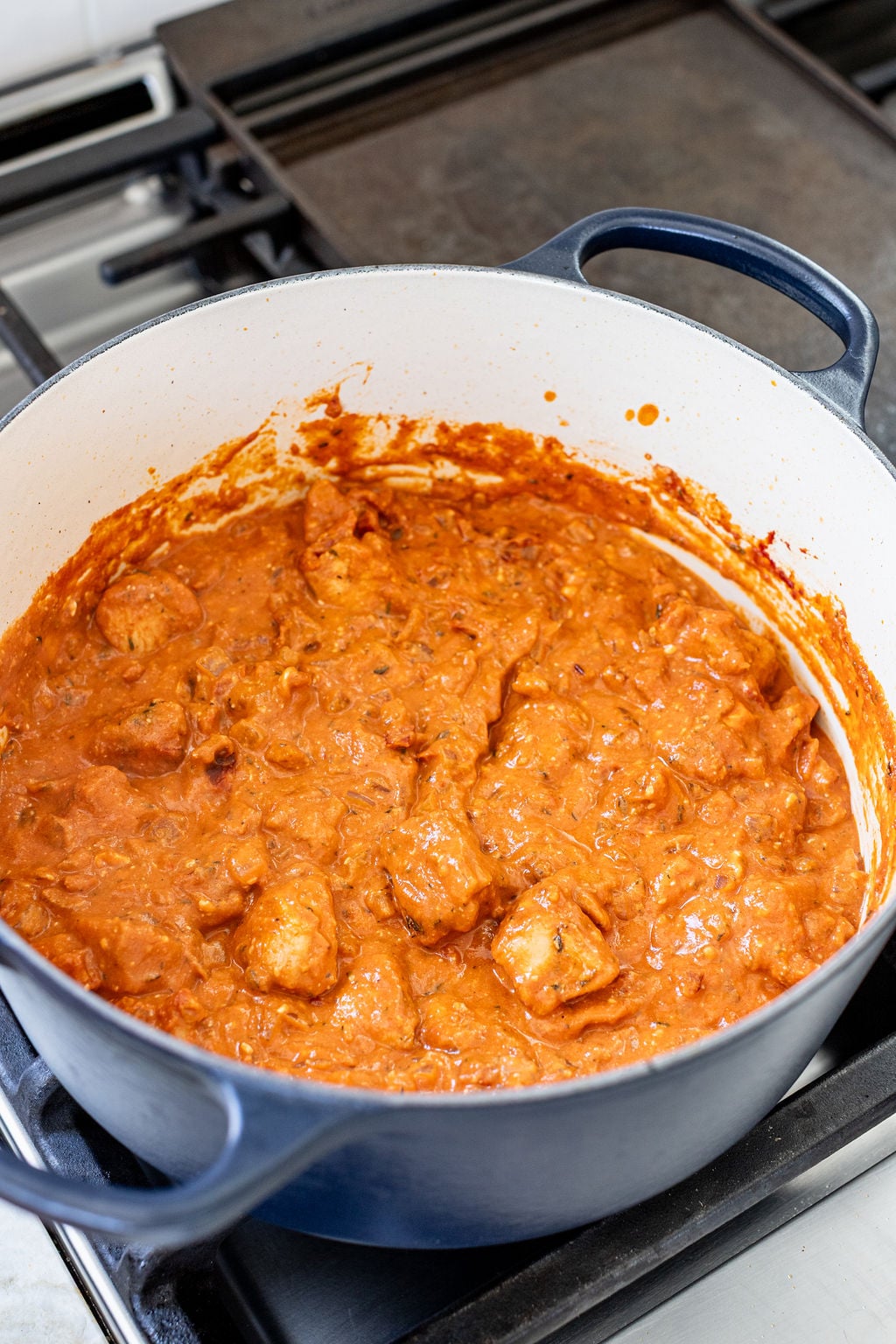 A light red creamy mixture with chunks of chicken in a large pot on a stove.
