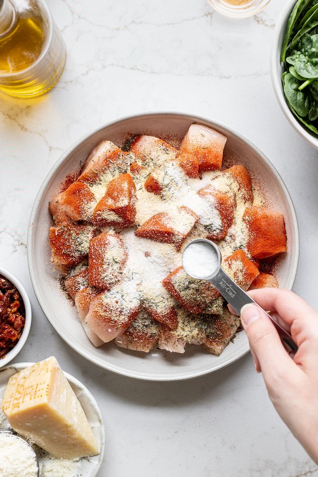 A hand pouring a tablespoon of salt over spiced, chopped chicken.