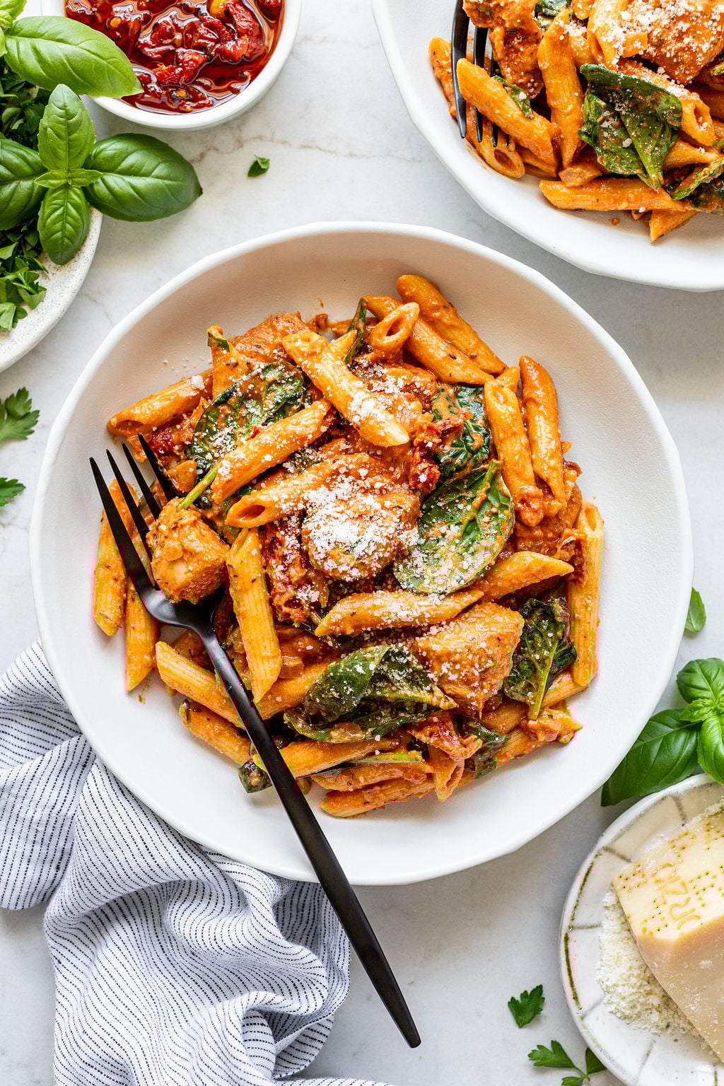 Creamy orange pasta, sundried tomatoes, spinach, and chunky chicken on a plate with a fork.