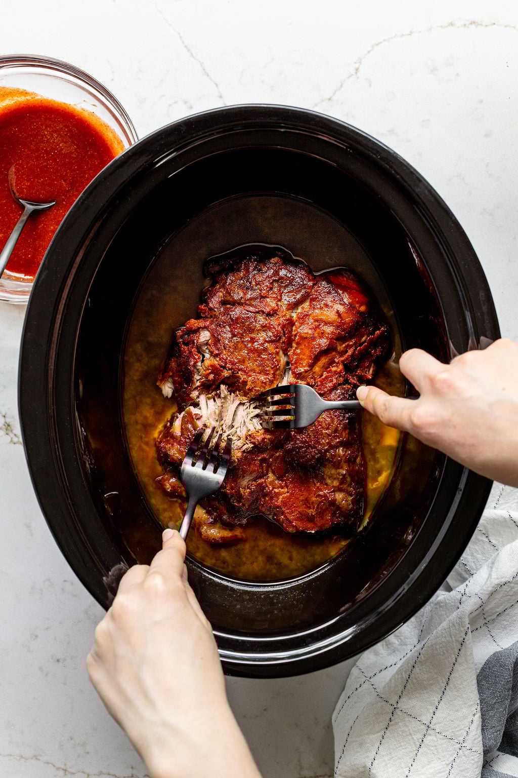 Two hands shredded cooked pork shoulder with two forks.