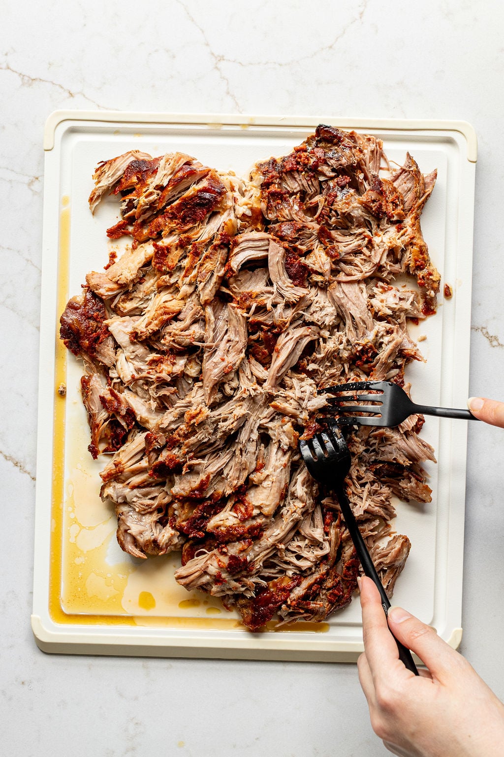 Hands shredding bbq pork with forks.