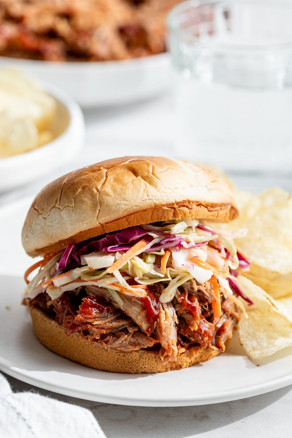 Coleslaw and juicy shredded pork with barbecue sauce in between burger buns on a plate.