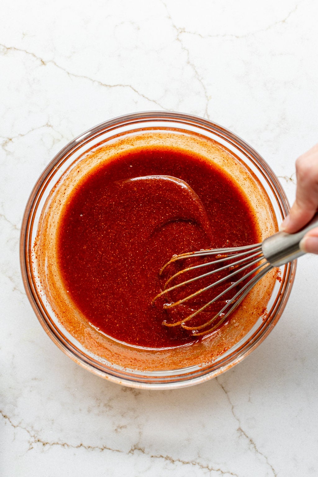 A hand whisking a thick red sauce in a mixing bowl.