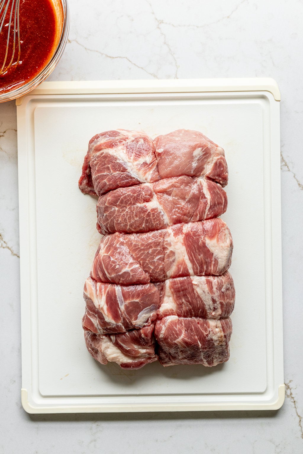 Five raw pork shoulders on a cutting board.
