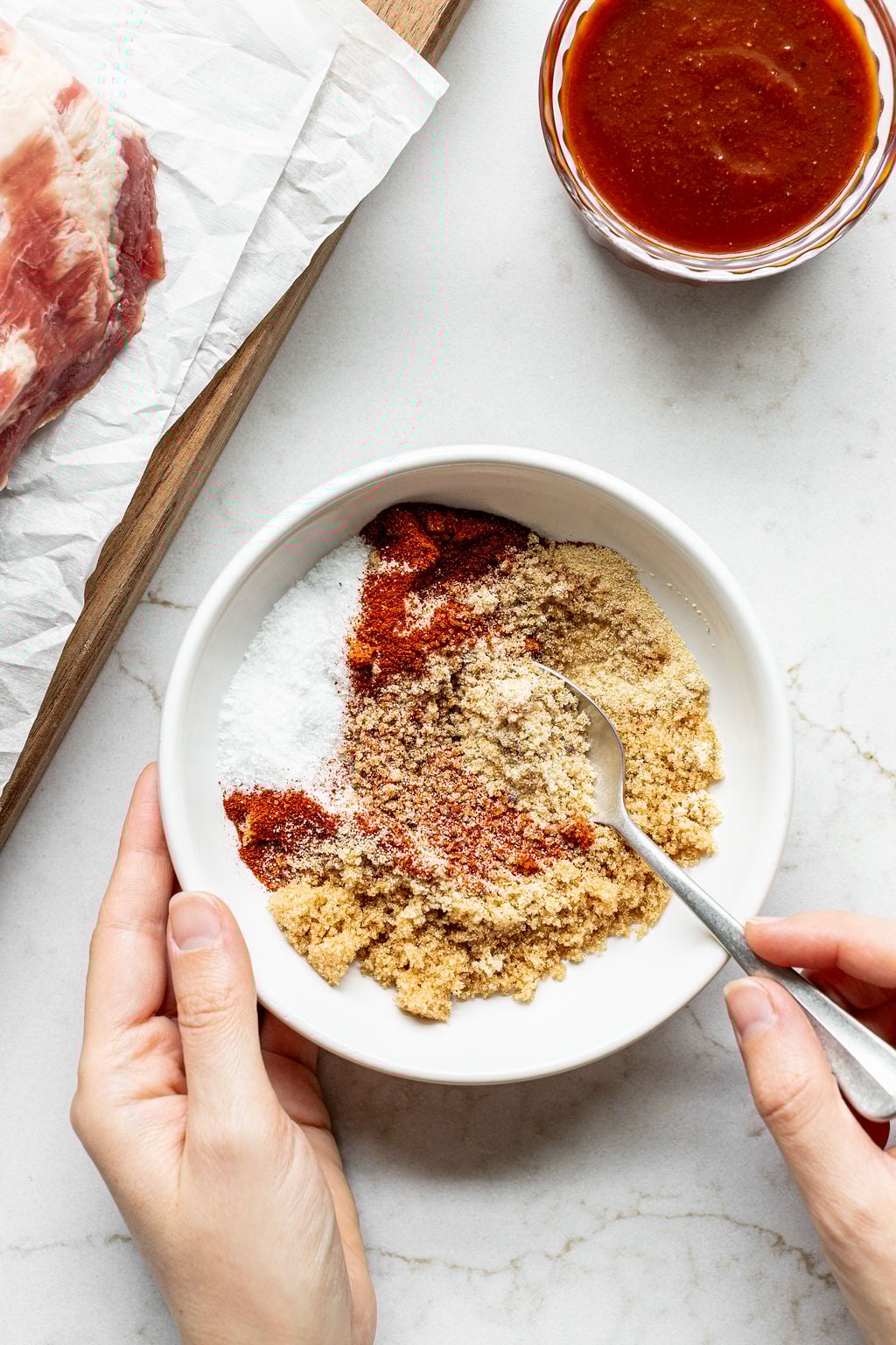 A hand stirring spices for a dry brown sugar rub in a bowl.