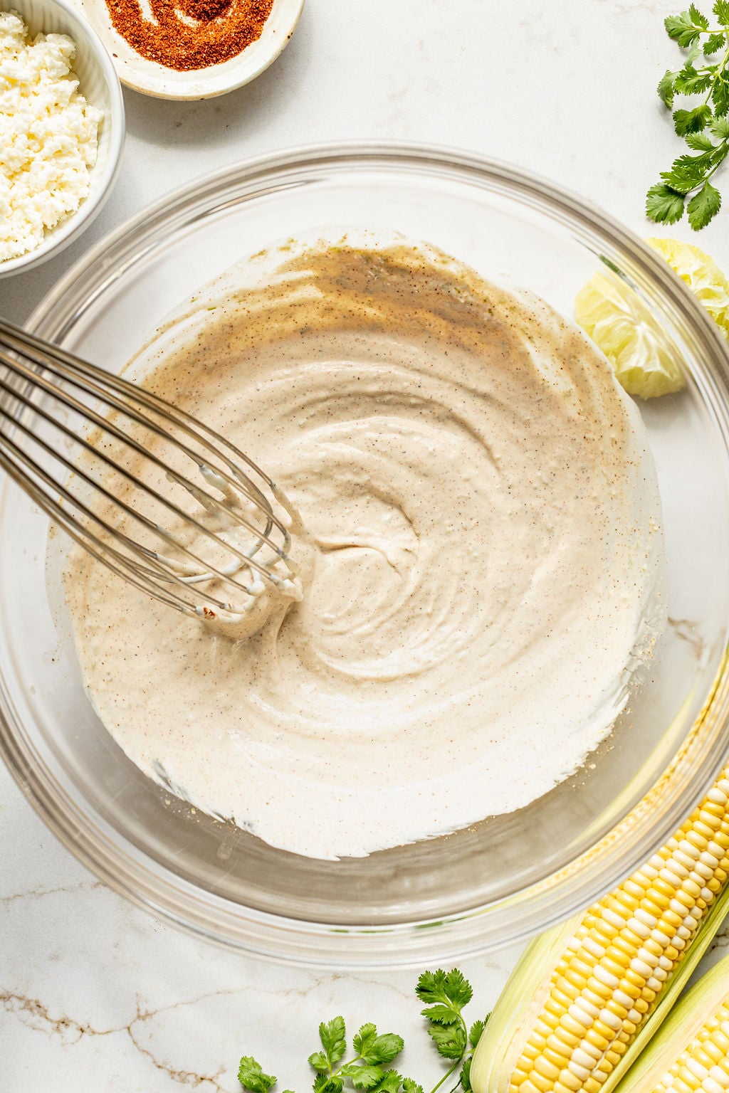 A whisk in a bowl of a creamy, light yogurt and spice mixture.