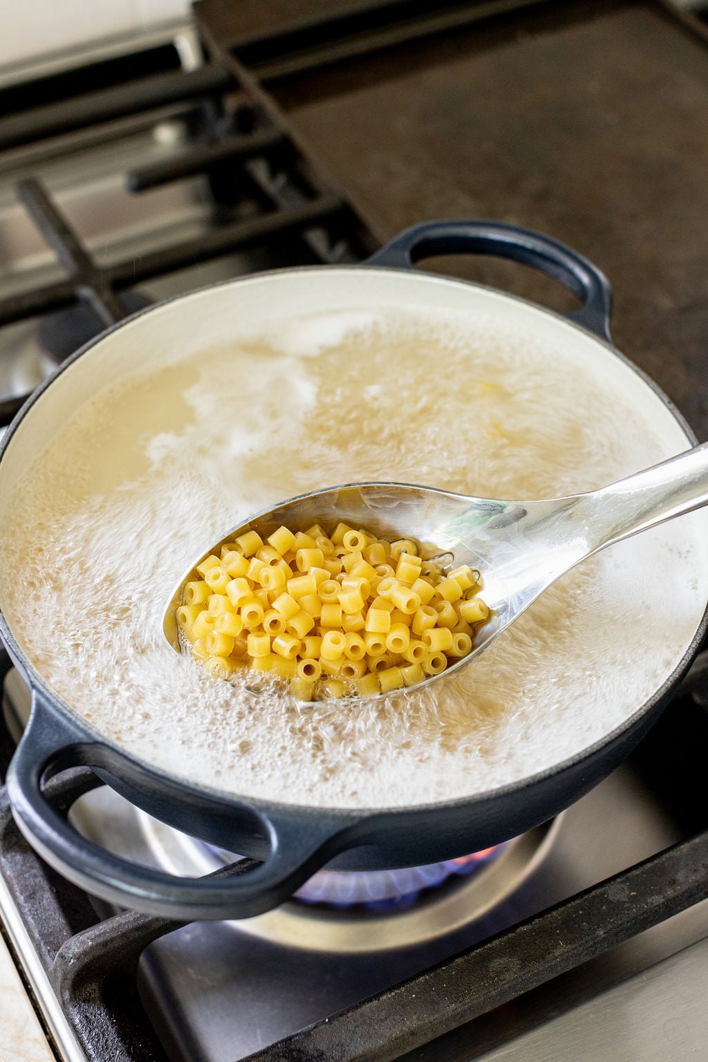 A spoon lifting cooked small-shaped pasta from a pot of boiling water.