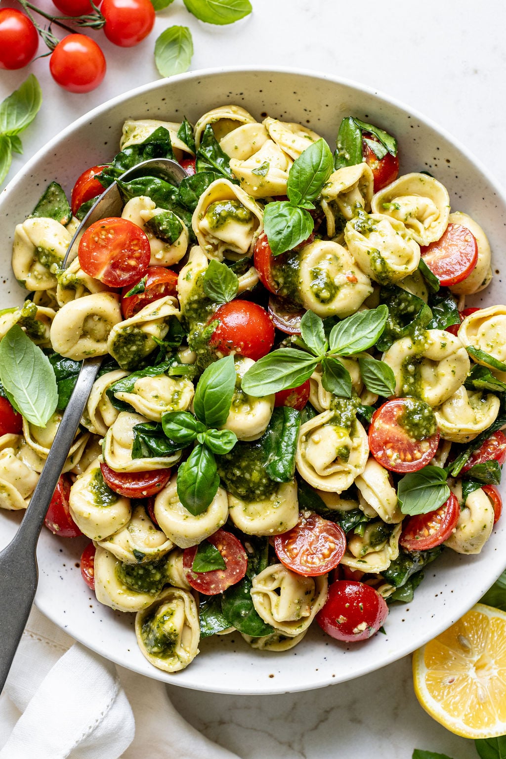 Creamy pesto, tortellini, basil, and cherry tomatoes in a bowl.