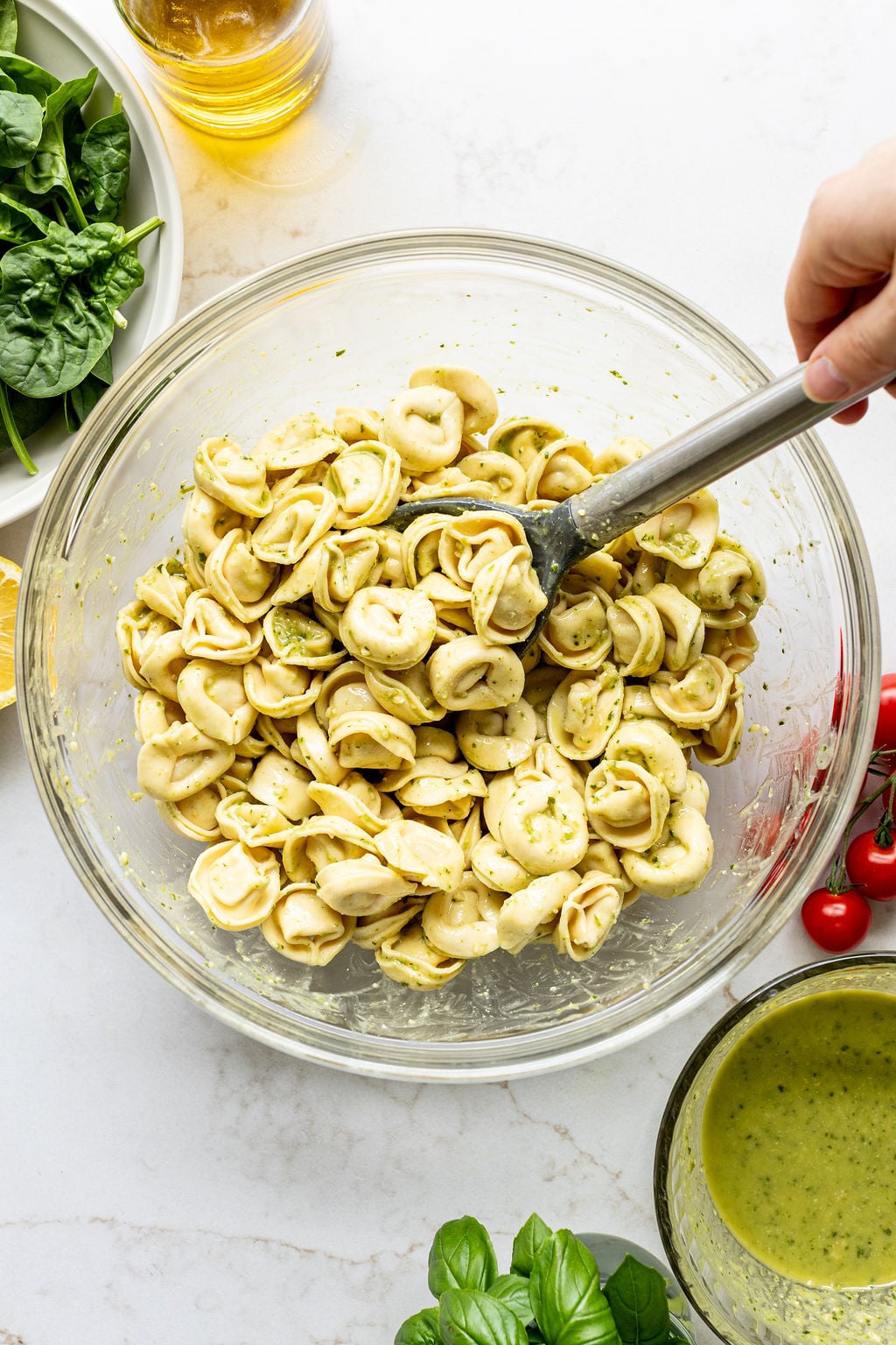 A hand stirring cooked tortellini and creamy pesto in a bowl.