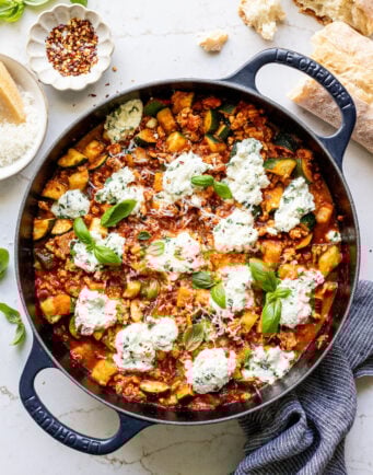 A skillet of ground turkey, diced zucchini, tomato sauce, and ricotta topped with fresh basil and parmesan.